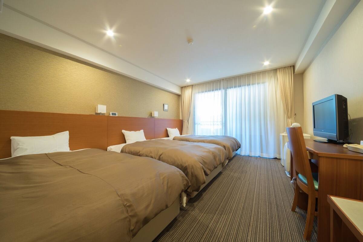 Quarto de hotel com duas camas, uma mesa de escritório com um computador e uma televisão.