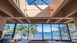 A room with large windows overlooking a beach, a skylight, and a view of the ocean. - Atami Onsen New Tomiyoshi (Atami)