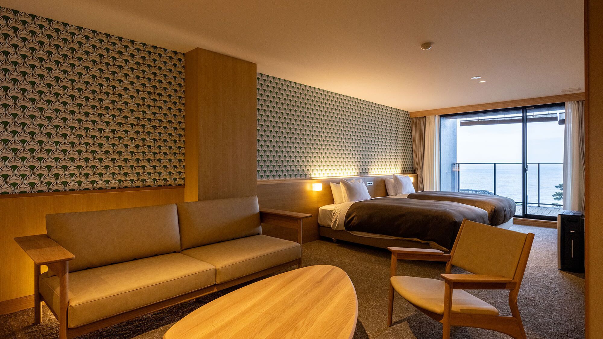 A hotel room with a sofa, a bed, a chair, and a view of the sea.