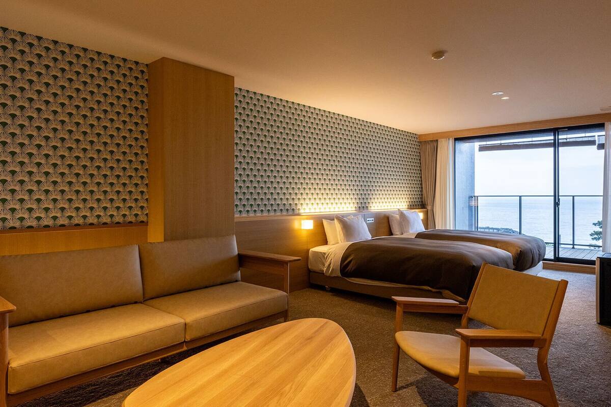 Quarto de hotel com sofá, cama, poltrona e vista para o mar.