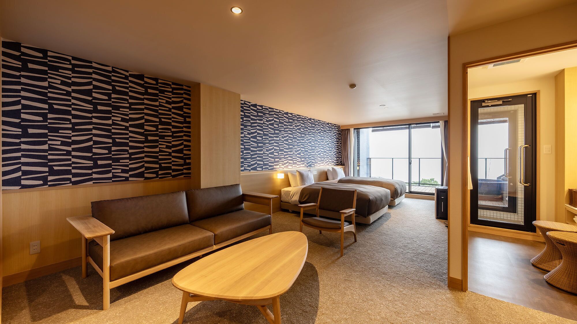 A modern hotel room with a sofa, a wooden coffee table, a bed with a view, and a patterned wall.