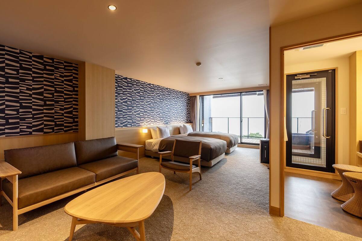 Quarto de hotel moderno com sofá, mesa de centro de madeira, cama com vista e parede com padrão.
