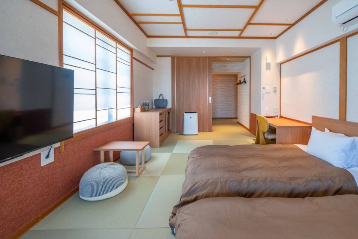 Quarto de hotel com cama, televisão, escrivaninha, cadeira, mesa pequena e frigorífico.