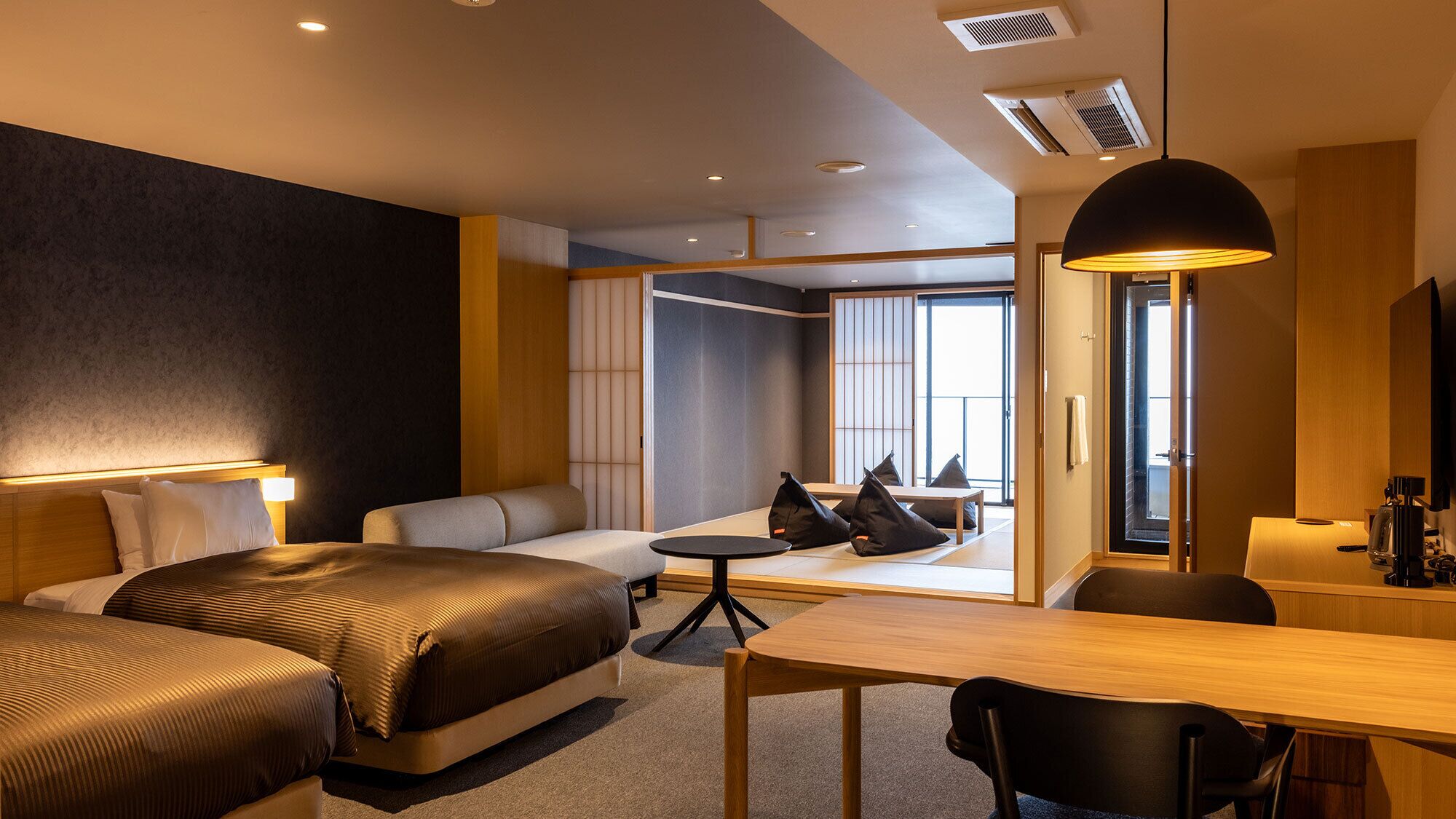 Une chambre d’hôtel moderne équipée d’un lit, d’un canapé, d’un bureau et offrant une vue sur l’extérieur grâce à une grande fenêtre.