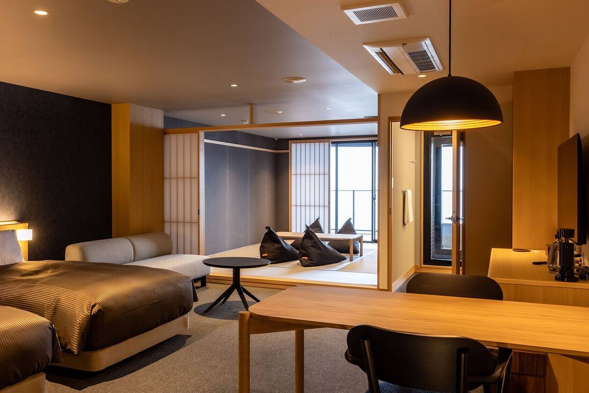 Quarto de hotel moderno com cama, sofá, escrivaninha e vista através de uma grande janela.