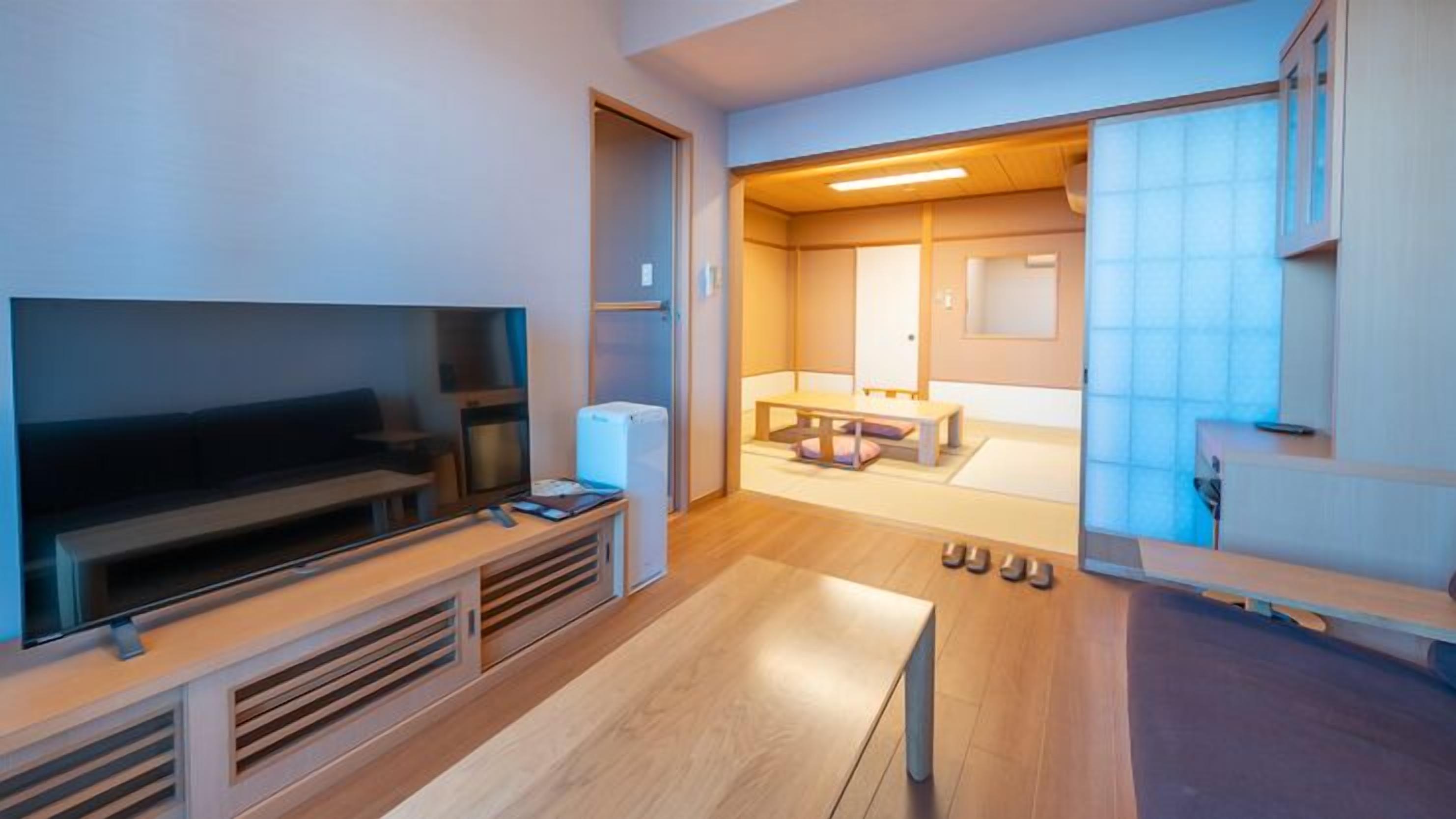 A modern living room with a flat-screen TV, a small refrigerator, and a wooden coffee table.