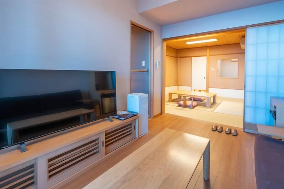 A modern living room with a flat-screen TV, a small refrigerator, and a wooden coffee table.
