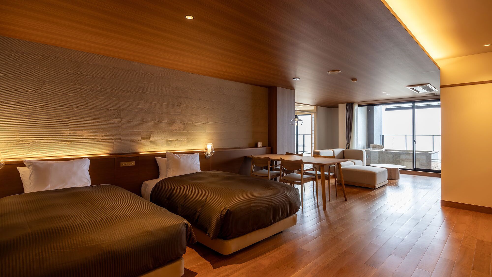 A hotel room with two beds, a dining area, and a balcony with a view.
