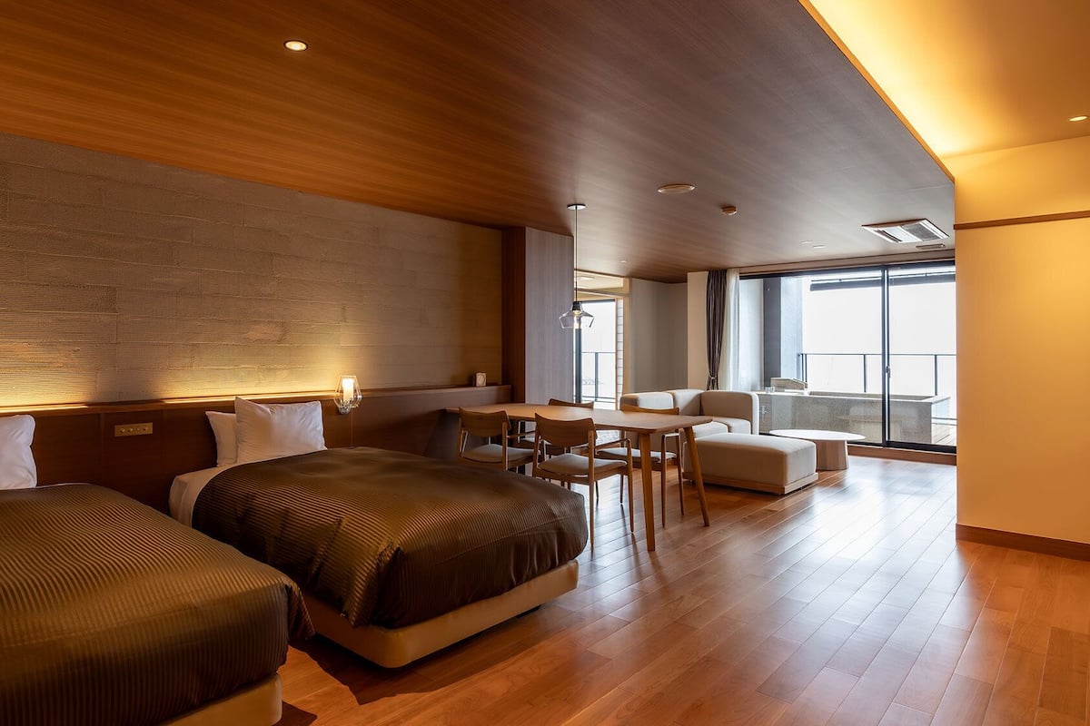 Quarto de hotel com duas camas, área de refeições e varanda com vista.