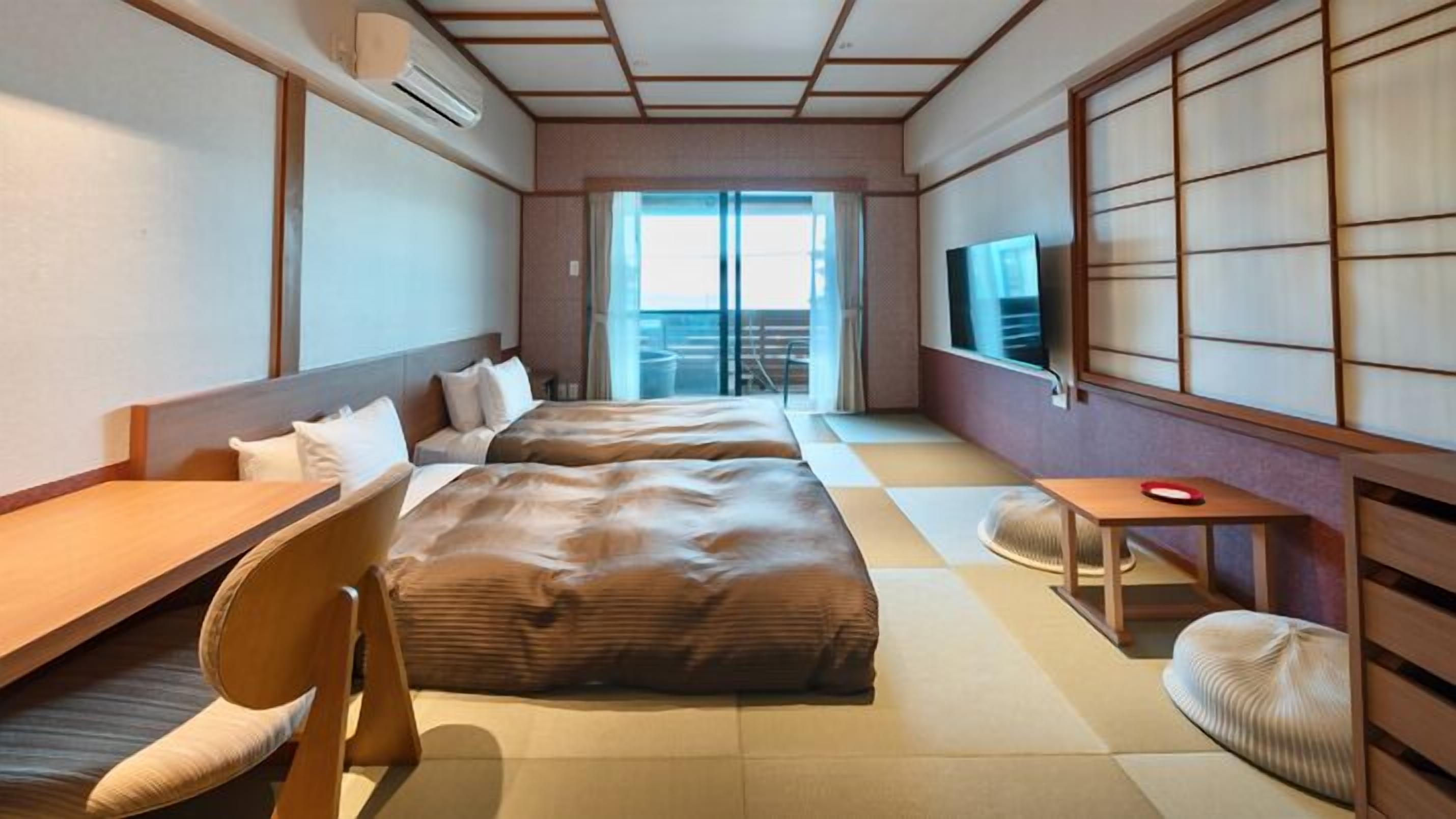Une chambre d’hôtel comprenant un lit, une chaise, une petite table, un téléviseur et une porte coulissante donnant sur un balcon.