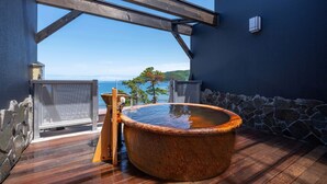 A hot tub on a wooden deck with a stone wall and a view of the sea. - Atami Onsen New Tomiyoshi (Atami)