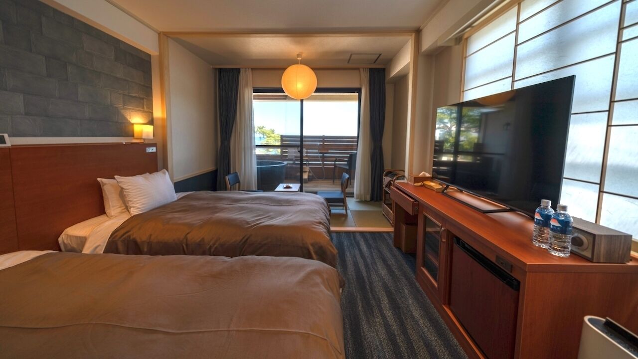 Une chambre d’hôtel avec deux lits, une télévision, un bureau et un balcon avec des meubles d’extérieur.