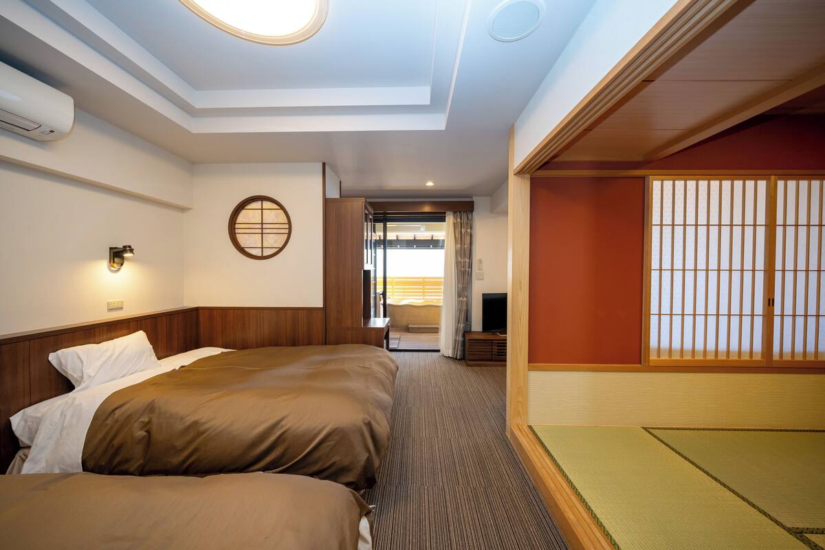 Quarto de hotel com cama, televisão, ar-condicionado fixado na parede e porta deslizante para uma varanda.