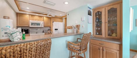 A kitchen with wooden cabinets, a microwave, a stove, and a bar stool.