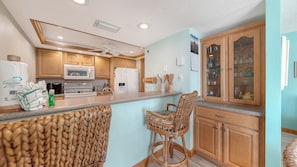 Une cuisine avec des meubles de rangement en bois, un four à micro-ondes, une cuisinière et un tabouret de bar.