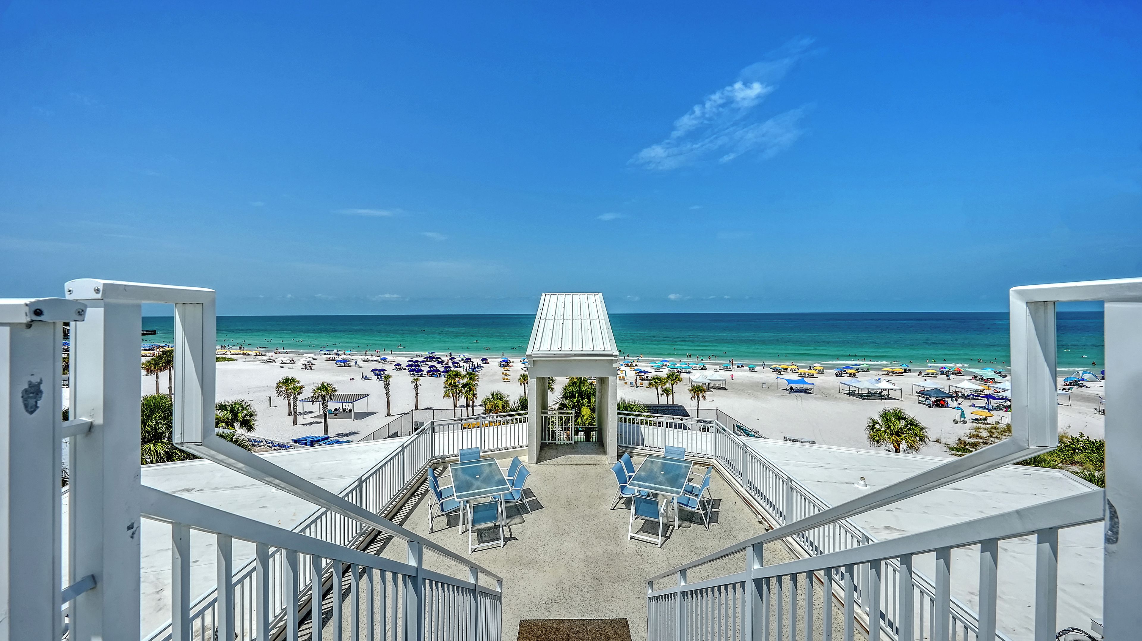 A beach view from a balcony with a clear sky, a sandy beach, and a pavilion.