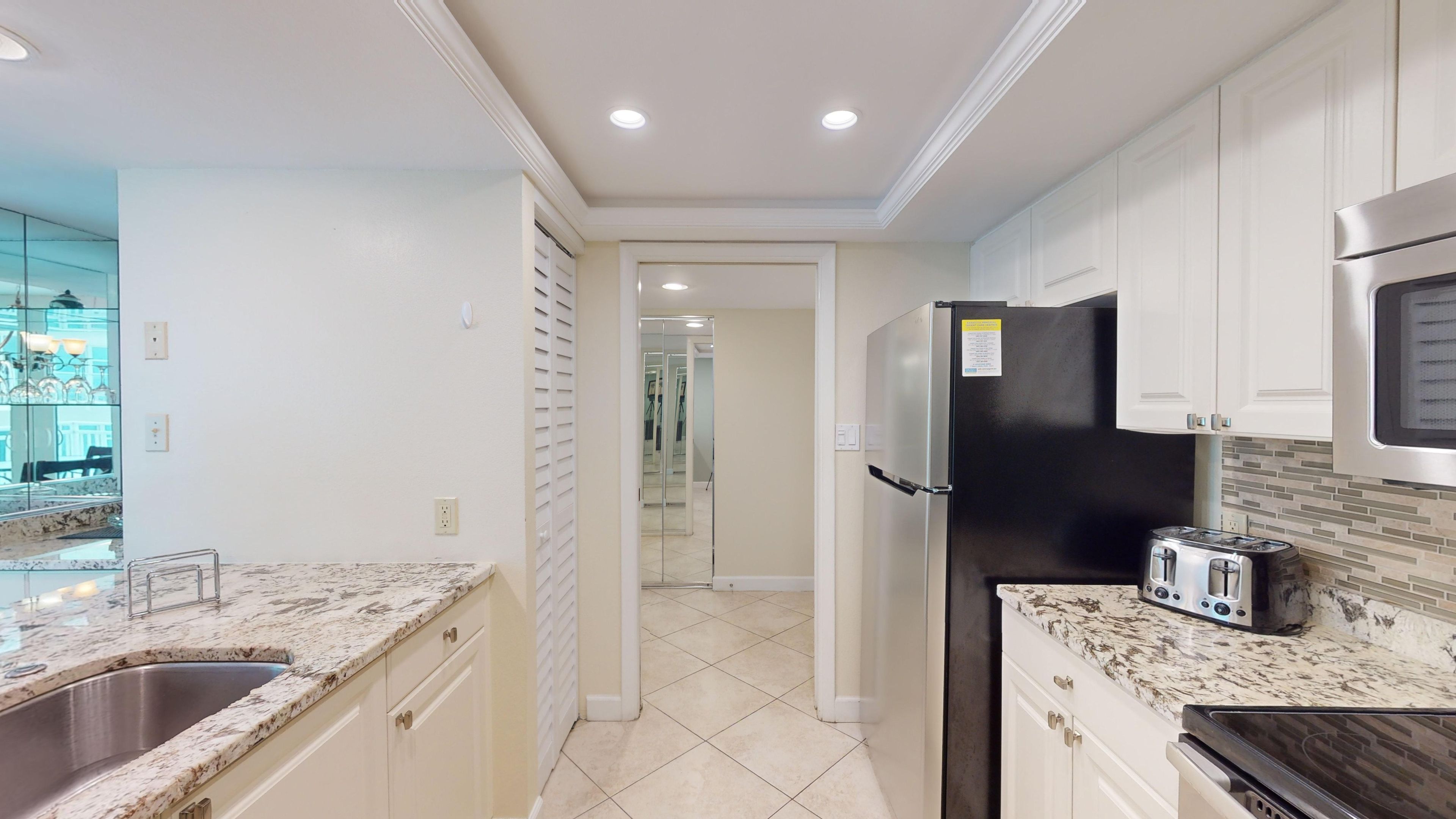 A modern kitchen with white cabinetry, a black refrigerator, a stainless steel sink, and a tiled backsplash.