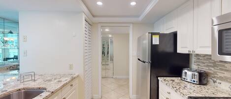 A modern kitchen with white cabinetry, a black refrigerator, a stainless steel sink, and a tiled backsplash.
