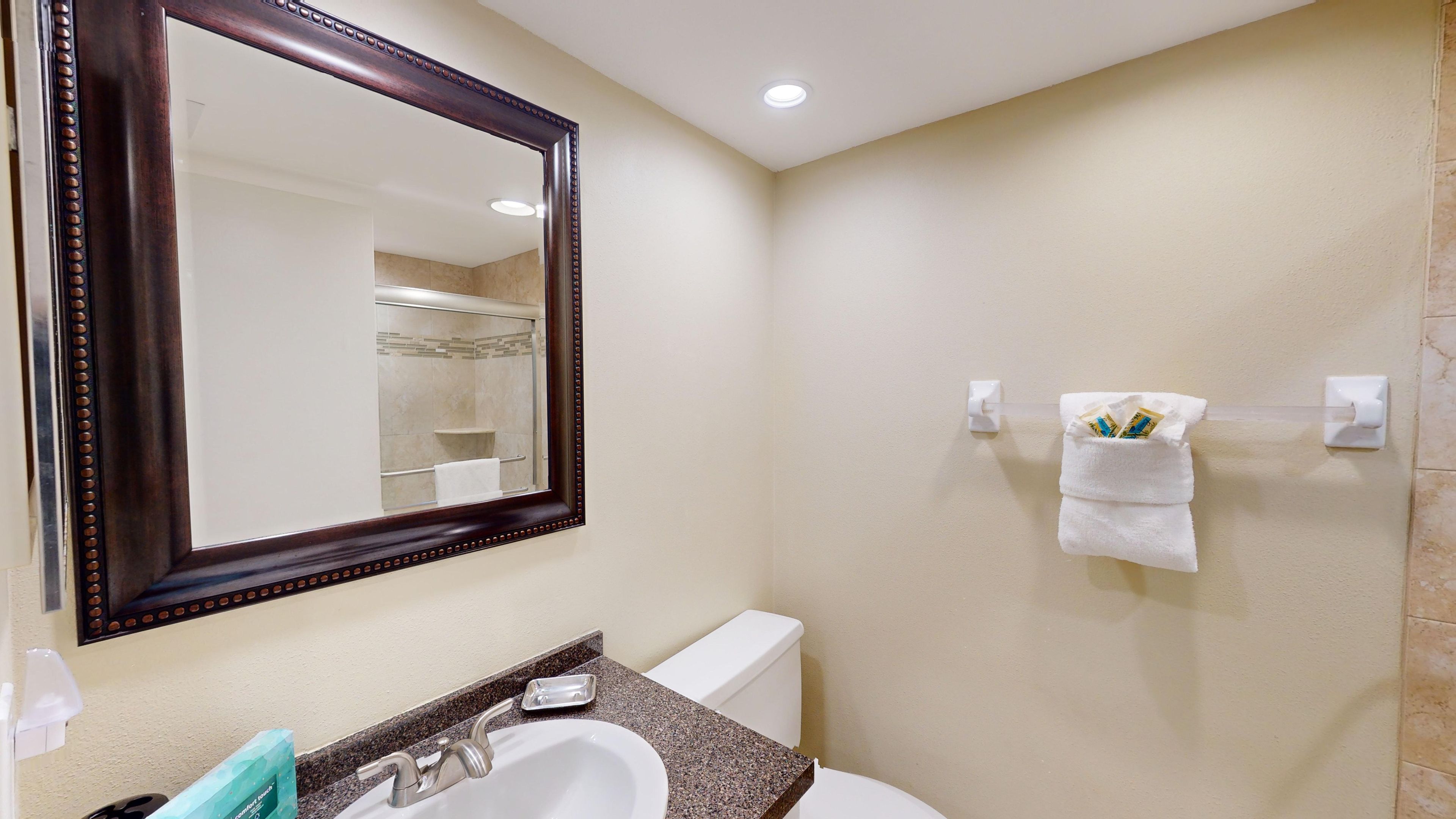 A bathroom with a large mirror, a sink, a toilet, and a towel rack with towels.