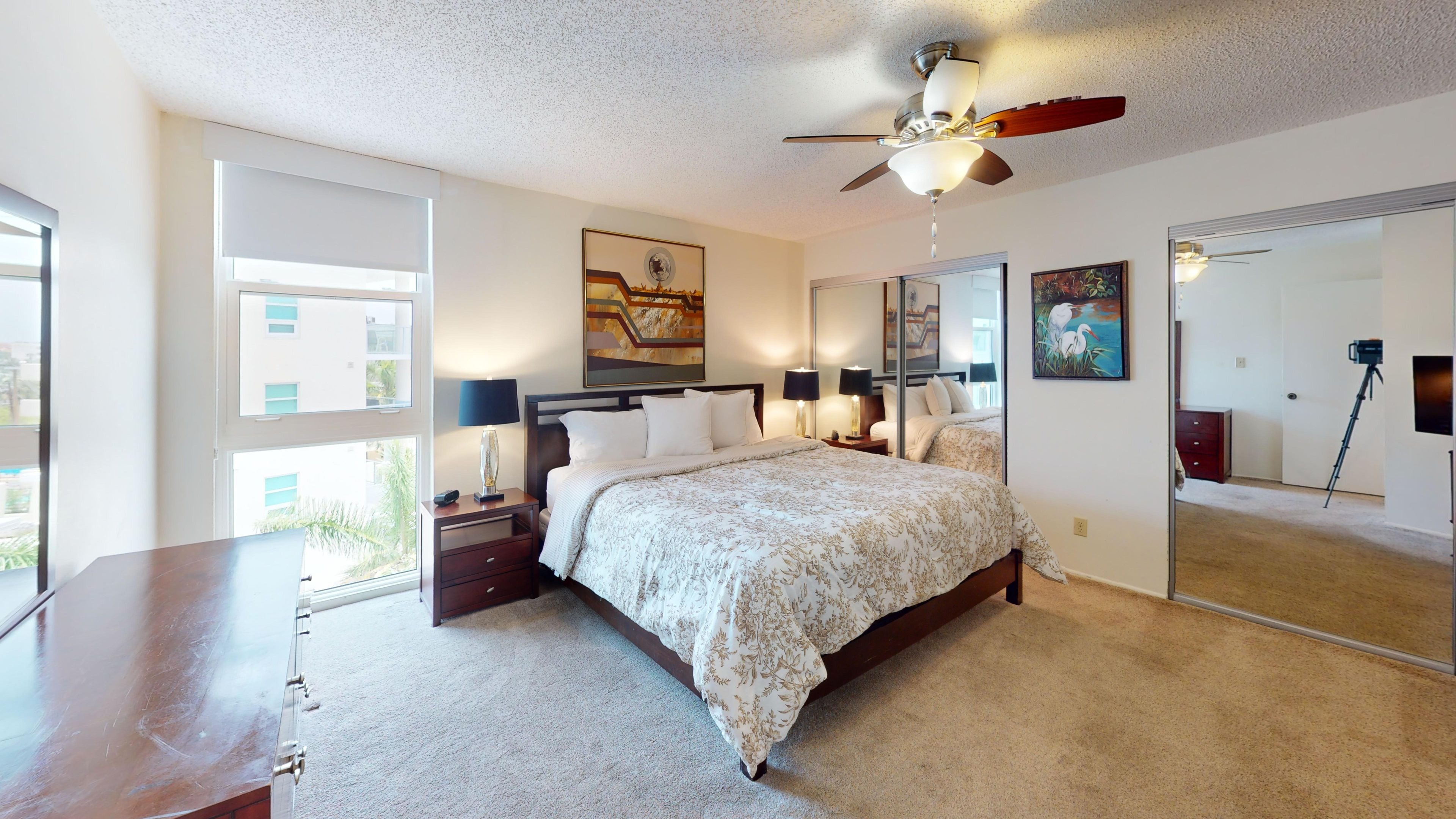 A bedroom with a bed, nightstands, a ceiling fan, and a large mirror.