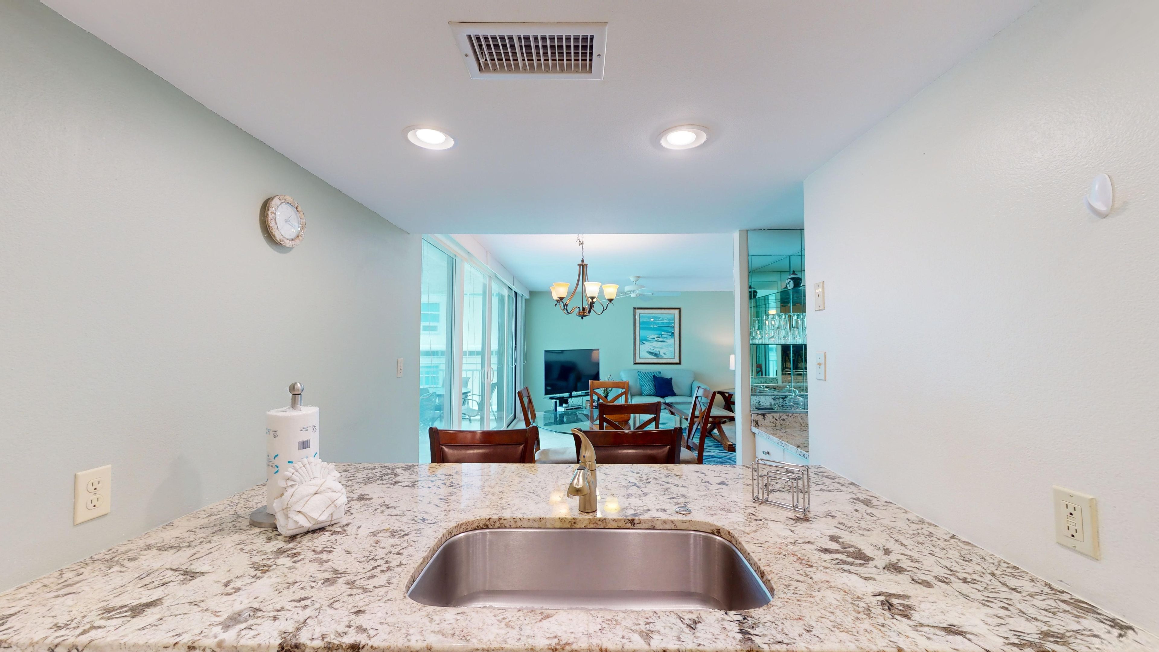 A kitchen with a granite countertop, stainless steel sink, and a dining area with a table and chairs.