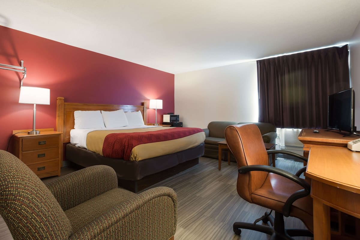 A hotel room with a bed, a desk, a chair, a TV, and a lamp.