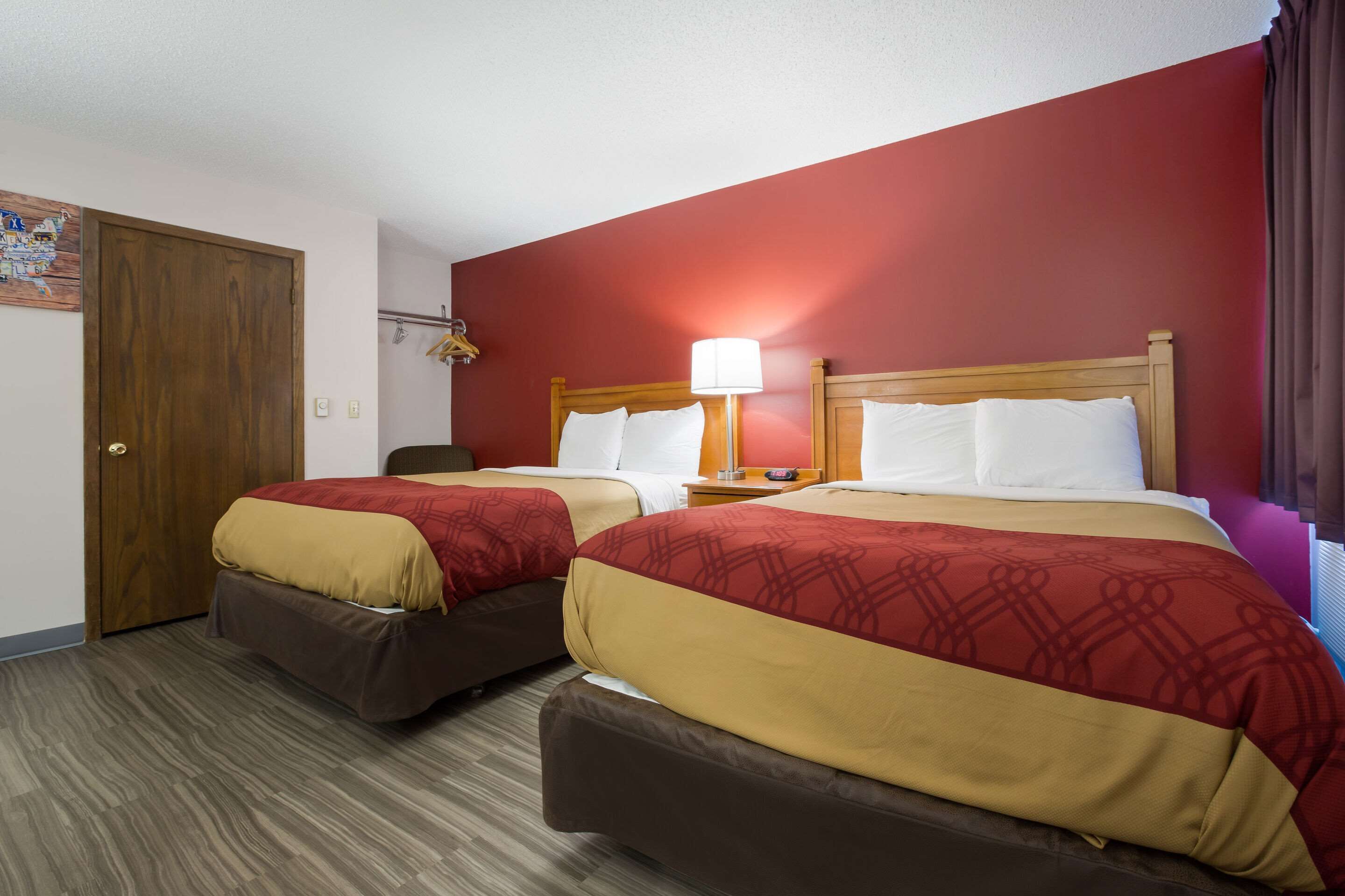 Habitación de hotel con dos camas, cada una con cabecera de madera, pared roja y suelo de madera.