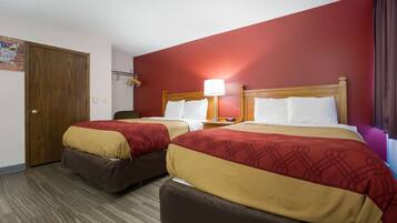Habitación de hotel con dos camas, cada una con cabecera de madera, pared roja y suelo de madera.