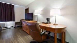Une chambre d’hôtel avec un bureau en bois, deux lampes, une télévision, une chaise, une commode et une fenêtre avec des rideaux.