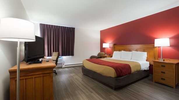 Une chambre d’hôtel comprenant un lit, des tables de chevet, un bureau avec une lampe, une télévision et une fenêtre avec des rideaux.