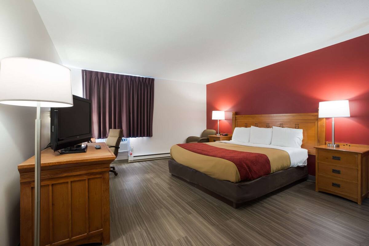 A hotel room with a bed, bedside tables, a desk with a lamp, a television, and a window with curtains.
