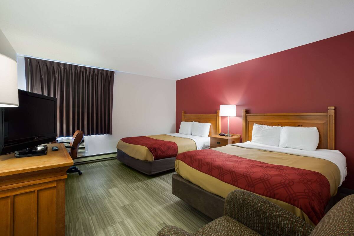 A hotel room with two beds, a desk with a television, and a window with curtains.