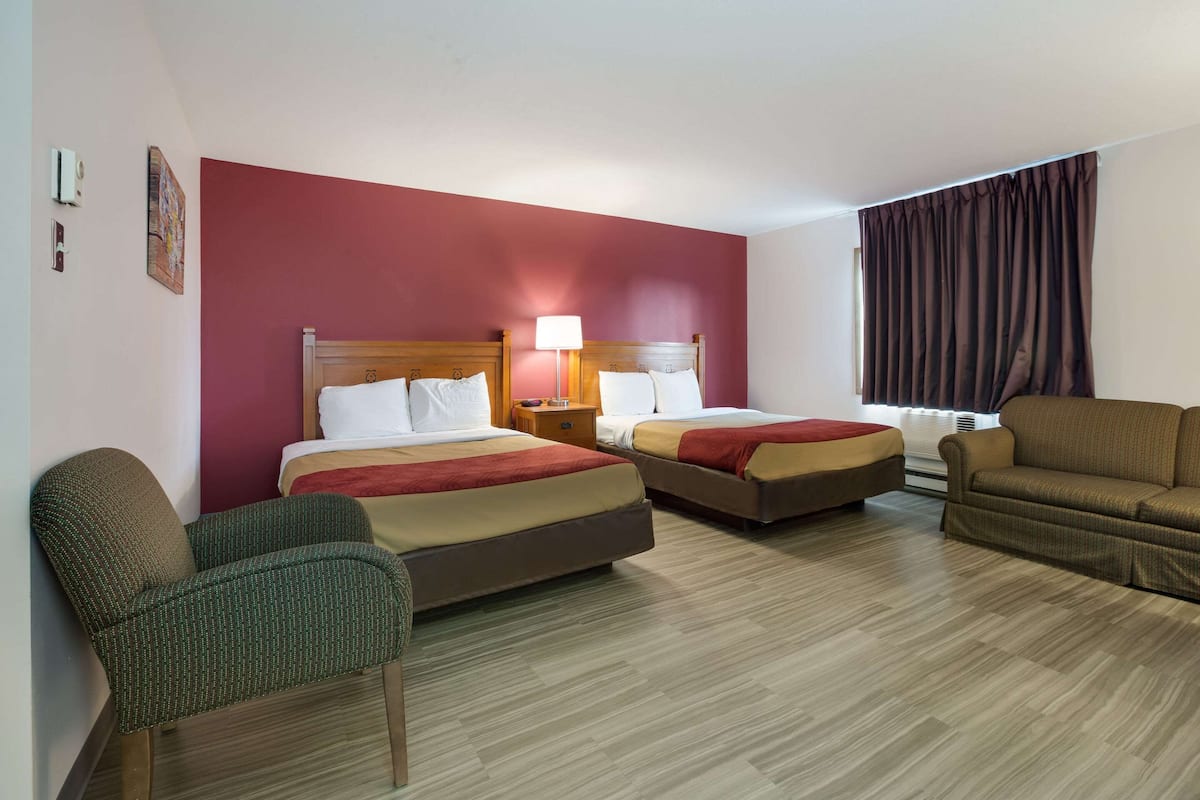 A hotel room with two beds, a sofa, a chair, and a window with curtains.