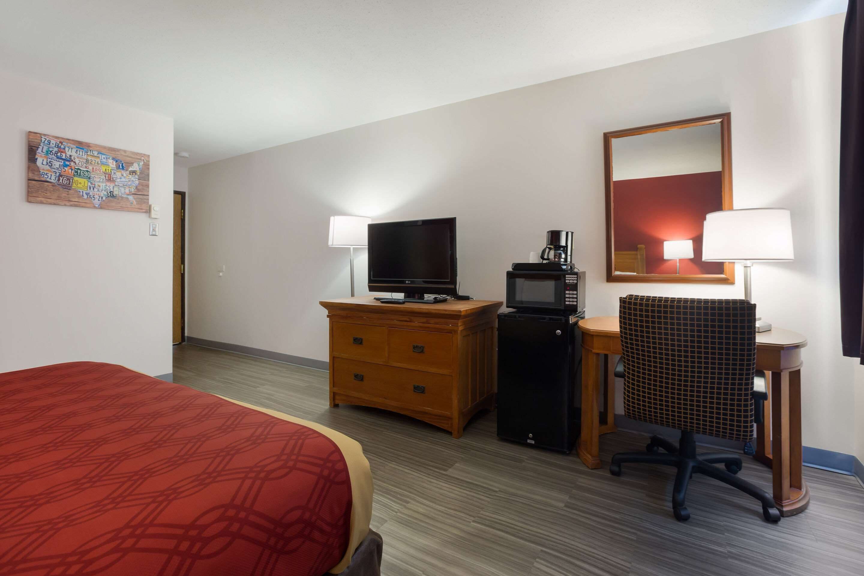 A hotel room with a bed, a desk with a computer, a television, a coffee maker, and a mirror.