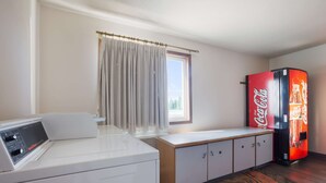 Un espace buanderie comprenant un lave-linge, un sèche-linge, un meuble de rangement, une fenêtre avec des rideaux et un réfrigérateur Coca-Cola.