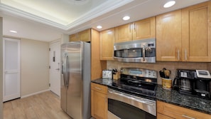 A modern kitchen with stainless steel appliances, wooden cabinets, and a granite countertop. - House Of The Sun #216GF (Sarasota)