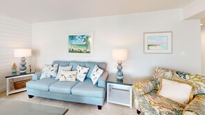 A living room with a light blue sofa, a patterned armchair, two side tables with lamps, and two framed landscape paintings on the wall. - House Of The Sun #402GS (Sarasota)