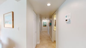 A hallway with a tiled floor, a painting on the wall, and a thermostat. - House Of The Sun #402GS (Sarasota)