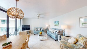 A modern living room with a television, sofas, a dining table, and a ceiling fan. - House Of The Sun #402GS (Sarasota)