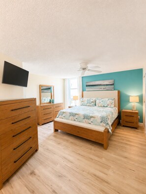 A bedroom with a bed, wooden dresser, bedside tables, a ceiling fan, and a television on the wall. - House Of The Sun #402GS (Sarasota)