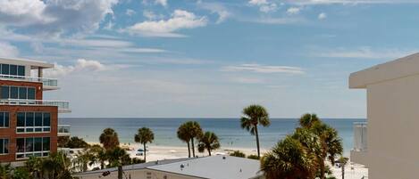 A beachfront property with a view of the ocean, palm trees, and adjacent buildings.