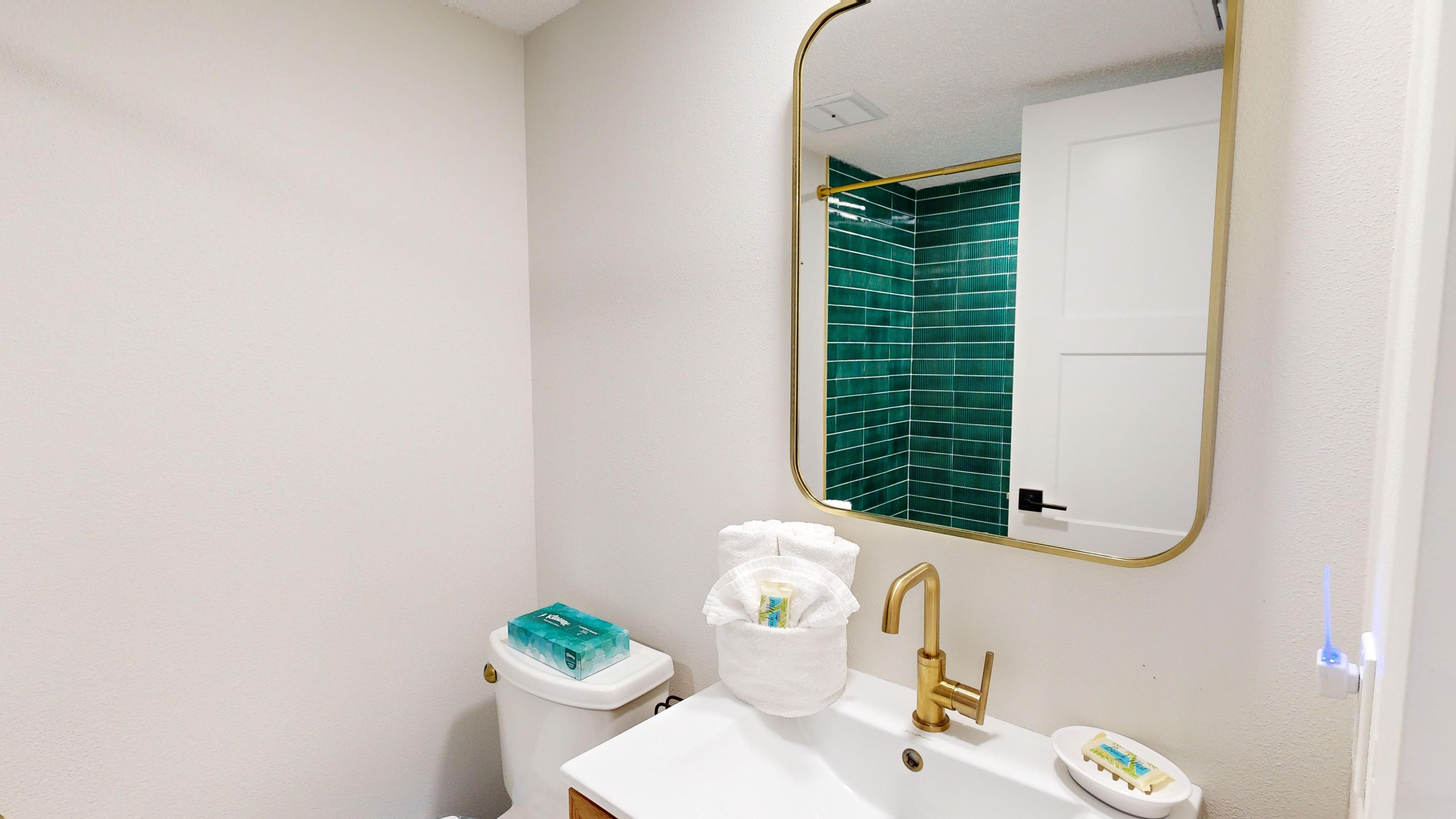 Un baño con lavamanos blanco, grifo dorado y espejo con marco dorado.