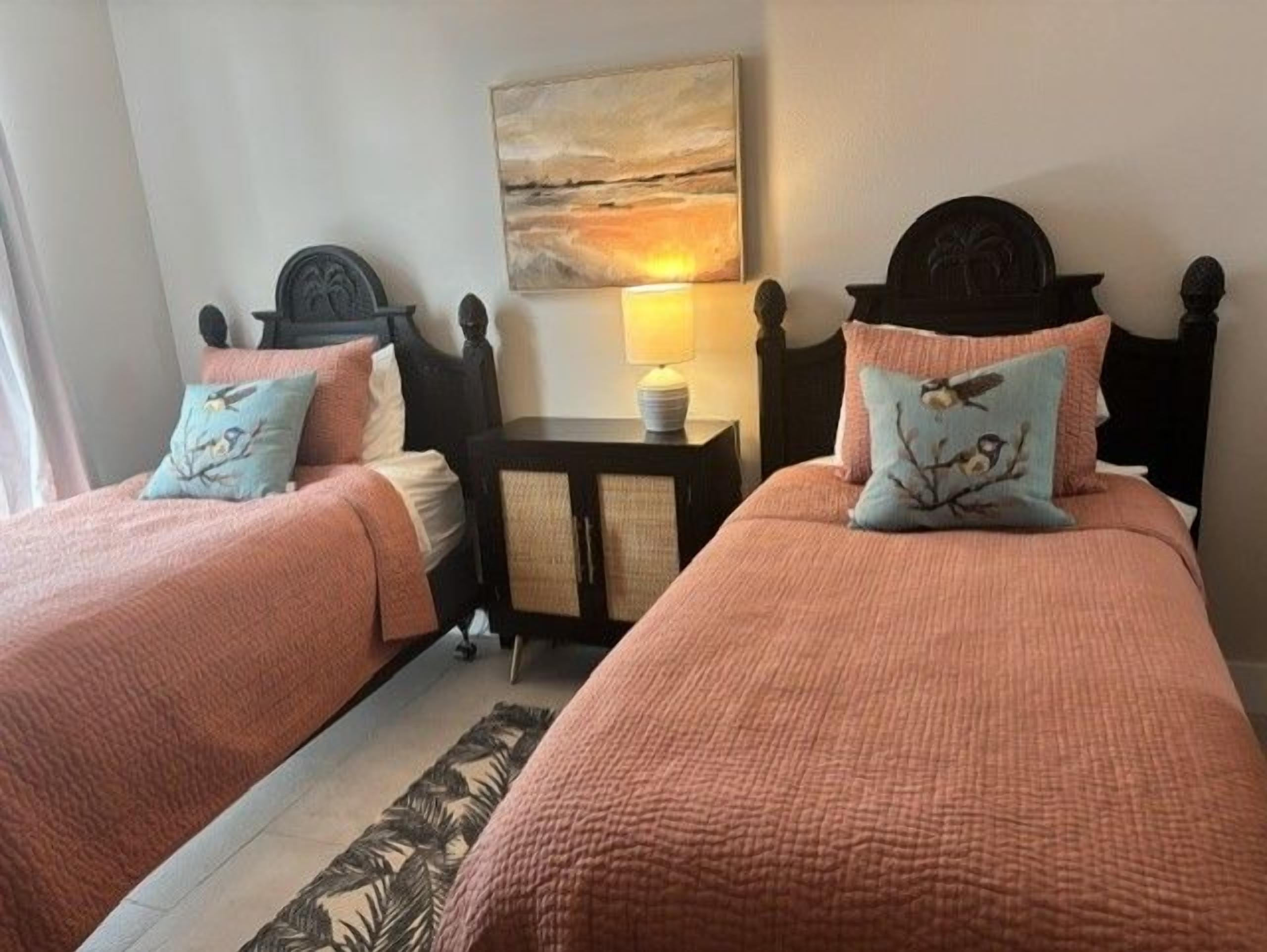 Een hotelkamer met twee bedden, een nachtkastje, een lamp en een schilderij aan de muur.