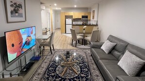 A living room with a TV, a sofa, a coffee table, and a dining area with chairs and a table. - ADELAIDE CBD APARTMENT - 3BR, 2BATH & CARPARK (Adelaide)
