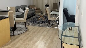 A modern living room with a sofa, chairs, a glass coffee table, and a dining area with a table and chairs. - ADELAIDE CBD APARTMENT - 3BR, 2BATH & CARPARK (Adelaide)