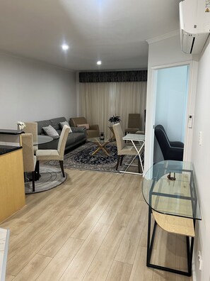 A modern living room with a sofa, chairs, a glass coffee table, and a dining area with a table and chairs. - ADELAIDE CBD APARTMENT - 3BR, 2BATH & CARPARK (Adelaide)