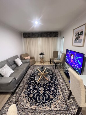 A living room with a grey sofa, a patterned rug, a coffee table, and a TV on a stand. - ADELAIDE CBD APARTMENT - 3BR, 2BATH & CARPARK (Adelaide)