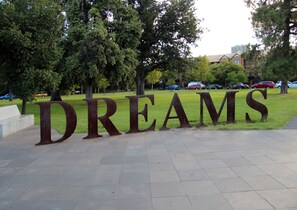A large metal sign with the word "DREAMS" in the foreground, set in a park with grass and trees in the background. - ADELAIDE CBD APARTMENT - 3BR, 2BATH & CARPARK (Adelaide)