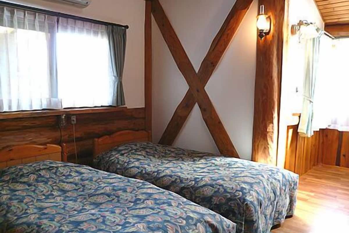 Una habitación con dos camas, vigas de madera, un ventanal con cortinas y una lámpara fijada a la pared.