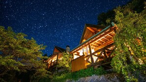 Eine Holzhütte, umgeben von Bäumen, vor einem Sternenhimmel.